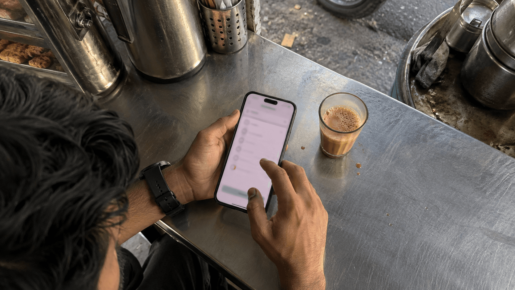 A person completes a short questionnaire on their phone beside a steaming glass of chai at a neighbourhood tea stall.